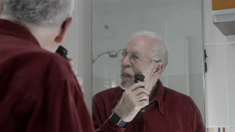 Old attractive man shaving in front of mirror in bathroom electric shaver Vídeos de archivo 230888196