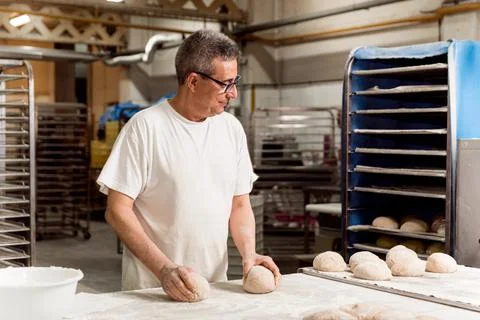 Old authentic baker in bakery making organic bread and taking care of it with Stock Photos