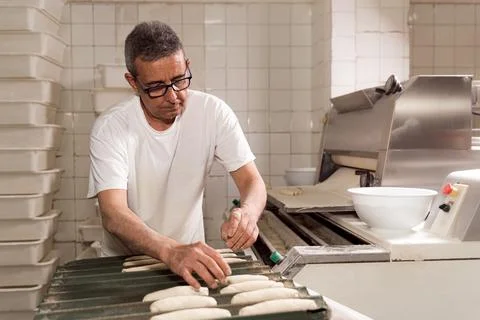Old authentic baker in bakery making organic bread and taking care of it with Stock Photos