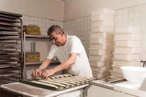 Old authentic baker in bakery making organic bread and taking care of it with Fotos Stock