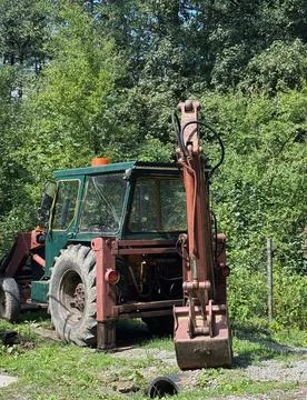 Old backhoe loader parked in a green wooded area. Stock Photos