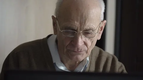 Old bald man sits at computer and looks for healthy advice Stock Footage 124667395