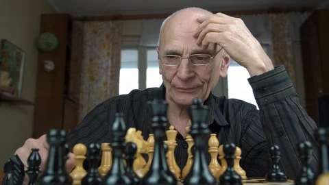 Old bald man thinks on hard knight chess figure move closeup Stock Footage 126766898