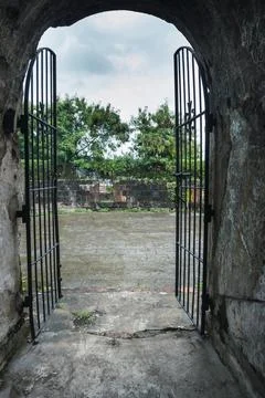 Old barred gate at the exit of an arched tunnel with a tree and vegetation in Stock Photos