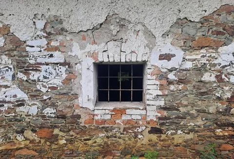 Old barred window in weathered stone and brick wall. Stock Photos