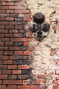 An old battered brick red wall with white plaster and a rusty broken bell Stock Photos