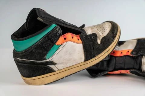 Old battered sneakers sit on a flat surface in an indoor space 스톡 사진