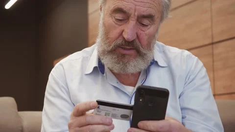 Old bearded man customer doing internet shopping. Holding credit card and makes  Stock Footage 148949764