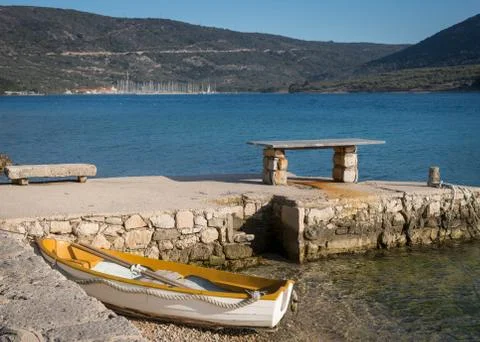Old bench and small rowing boat at the beach of Cres Stock Photos