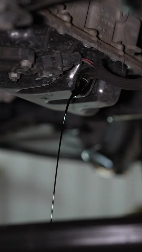 Old black engine oil drains from car into a container. Stock Footage 345707911