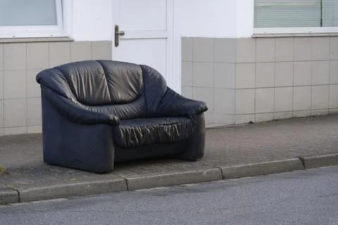 Old black leather two seats sofa left on the sidewalk outdoors Stock Photos