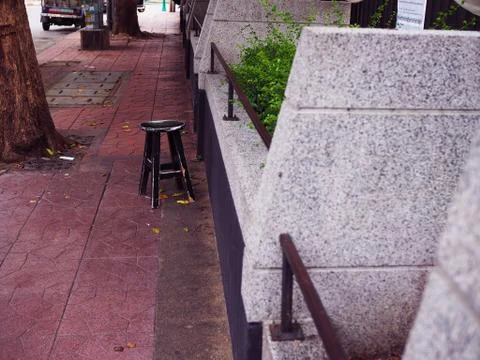 Old black stool on footpath, beside grey wall Foto stock
