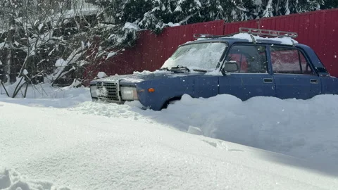 Old blue car standing in a snowdrift against a red fence in the countryside in w Vídeo Stock 306255643