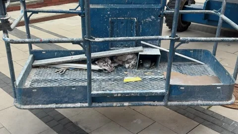 Old blue construction lift basket with tools and debris on a paved street Stock Footage 341830347
