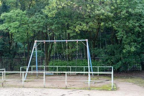 Old blue rusty swing set in an empty rural park playground Stock Photos