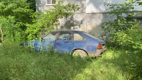 Old blue soviet car left near the house wall in bushes Stock Footage 278926172