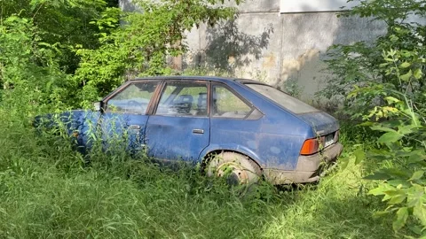 Old blue soviet car left near the house wall in bushes Stock Footage 278936241