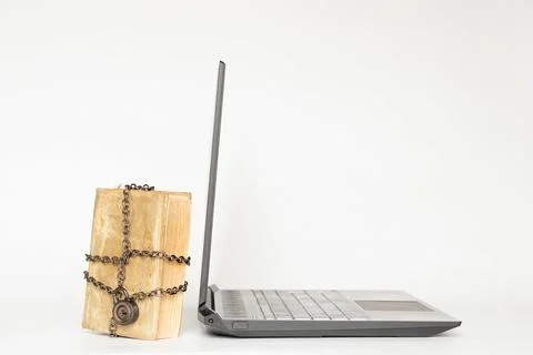 Old book in chains next to modern laptop on white background Stock Photos