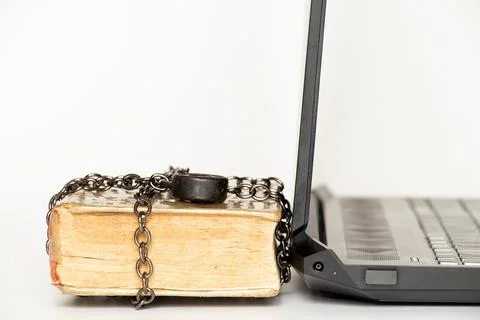 Old book in chains next to modern laptop on white background Stock Photos
