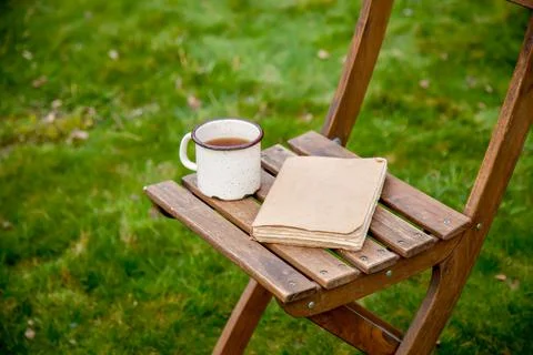 Old book with cup of tea on a table on green grass in spring Stock Photos