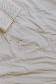 Old book opened on the bed with white bed sheets on the background. Top View. Stock Photos