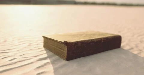Old book resting on soft sand under warm sunlight during afternoon hours Stock Illustration