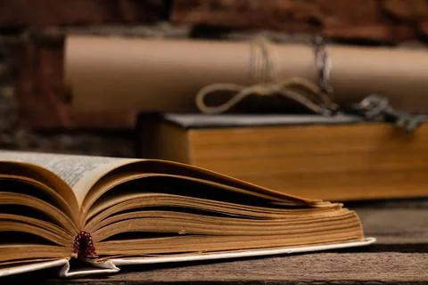 Old books with a scroll and key on a rustic wooden surface on a brick wall ba Foto stock