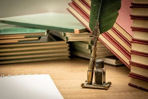 Old books stacked in disarray, an old pen with its ink and a notepad on an ol Stock Photos