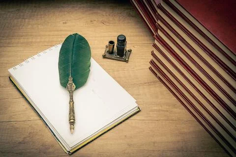 Old books stacked in disarray, an old pen with its ink and a notepad on an ol Stock Photos