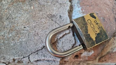 Old brass padlock on a stone wall. Rusty metal lock representing security and Stock Photos