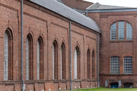 Old brick building with many windows, situated next to a green field Fotos de archivo