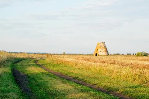 An old brick building stands alone in a field. An old dilapidated mill Stock Photos