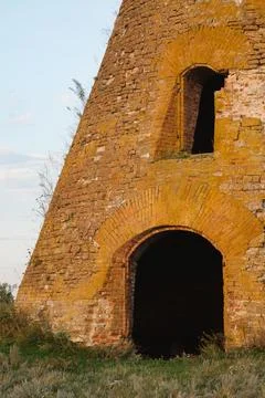 An old brick building stands alone in a field. An old dilapidated mill Stock Photos