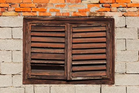 Old brick building wall with window covered with closed wooden blinds Stock Photos