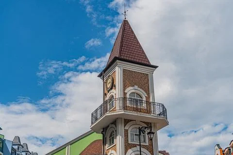 Old brick clock tower with pointed roof, square structure, white window frame Stock Photos