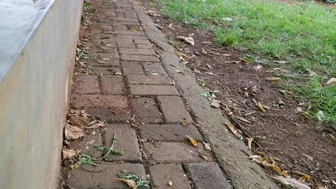 Old brick sidewalk next to grass and dirt path Stock Photos