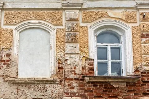 Old brick wall with cracked plaster, one arched window bricked up, another wi Foto stock
