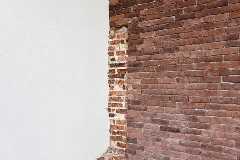 An old brick wall partially exposed behind a layer of white plaster Stock Photos