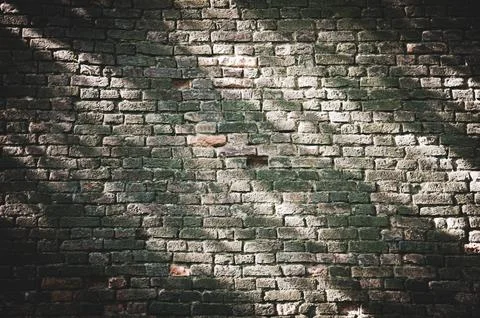 Old brick wall with rays of sun on it, urban background. Stock Photos