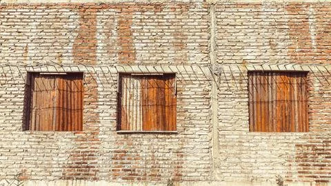 Old brick wall with three rusty corrugated metal-covered windows, showing w.. Stock-Fotos