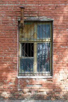 Old brick wall with window. Window has a grate and a chimney. Stock Photos