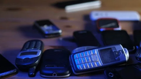 Old broken and dusty cell phones lie in a pile on the table in blue neon light. 動画素材 128095661