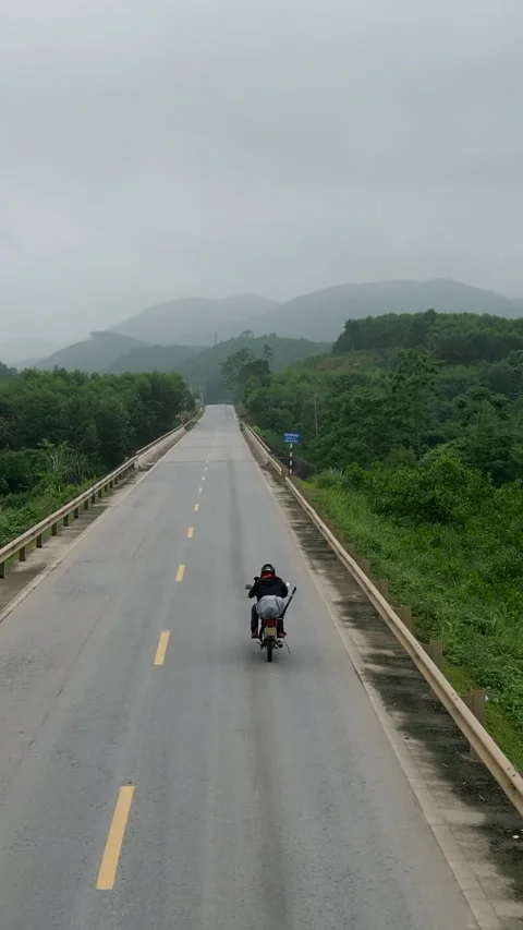 Old broken down motorcycle slowly driving on a narrow straight road in Vietnam Stock Footage 293612842