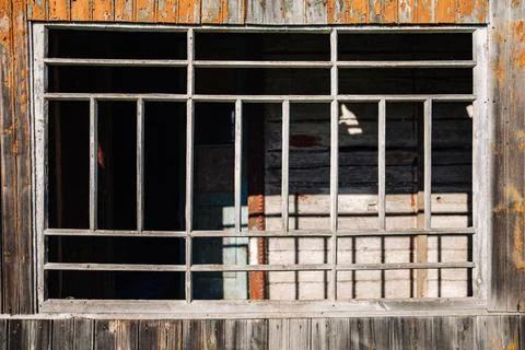 Old broken window with bars showing peeling paint on wooden wall Foto stock