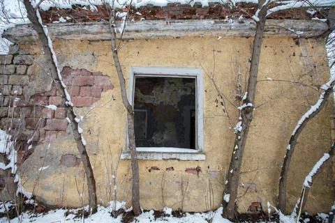 Old building with broken window surrounded by snow and trees in winter season Stock Photos