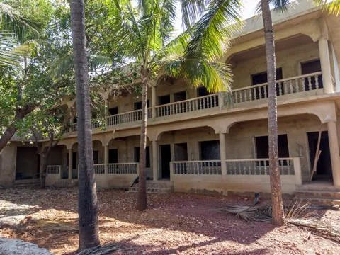 Old building with dark windows surrounded with trees. Shabby stony old house Stock Photos