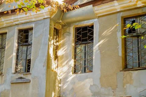 Old building facade with barred windows and peeling plaster bathed in warm .. Stock Photos
