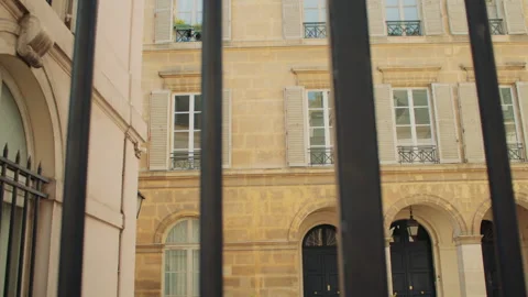 Old building facade with shuttered windows and balconies viewed through bars Stock Footage 313452694