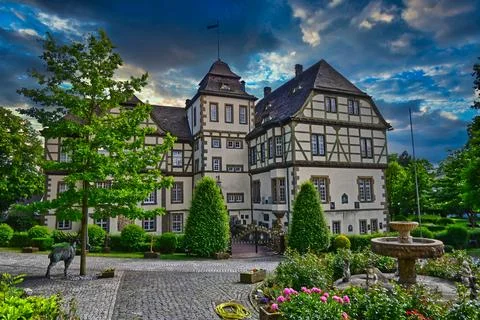 Old building surrounded by trees and garden near fountain under cloudy sky .. Stock Photos