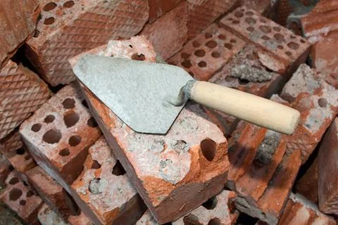 An old building tool, a trowel lying on a pile of red bricks Stock Photos